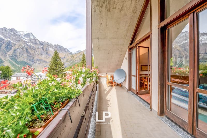 terraced balcony with potted plants, satellite dish, wooden deck, tiled floor, wooden doors, view of mountains and village
