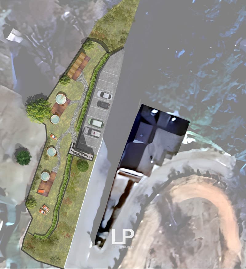 An aerial view of a landscape featuring a building and a parking area, with swimming pools and a view of the lake.