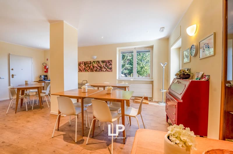Dining room with 4 tables, chairs, wooden floor, ceiling lamps, window with view, picture frame, fire extinguisher