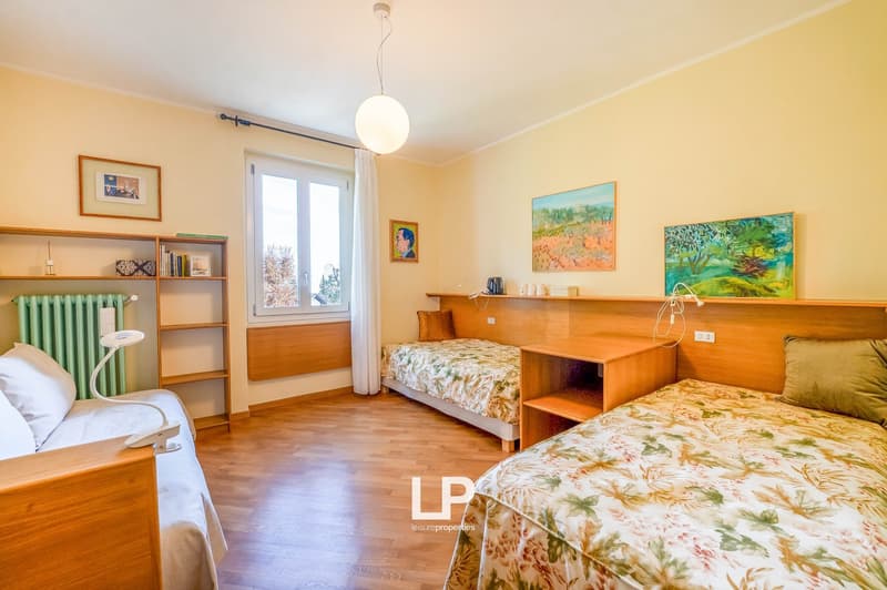 Three single beds, wooden floor, yellow walls, bookshelf, paintings, radiator, table lamp, bedside tables