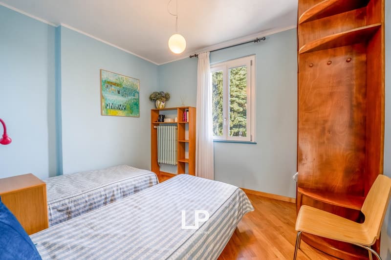 room with two single beds, wooden shelves, chair, radiator, picture on wall, window with curtain