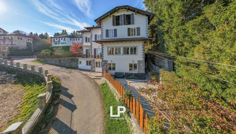 House with stone facade, glass windows, red roof, terrace, outdoor balcony, concrete driveway, stone fence, greenery surrounding.