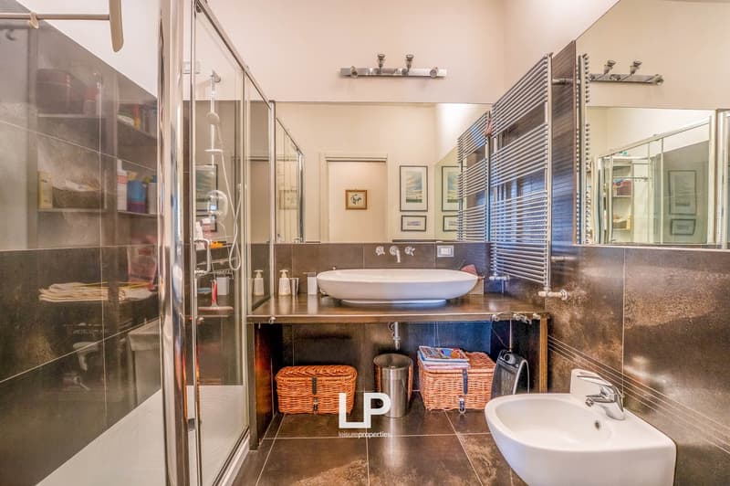 Glass shower stall, large mirror, double vanity with large basin and sink, baskets and a trash can, heated towel rack, tiled floor