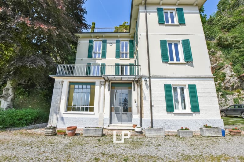 2 story house, white exterior, green shutters, large balcony on the second floor, garden with plants and gravel, car parked nearby