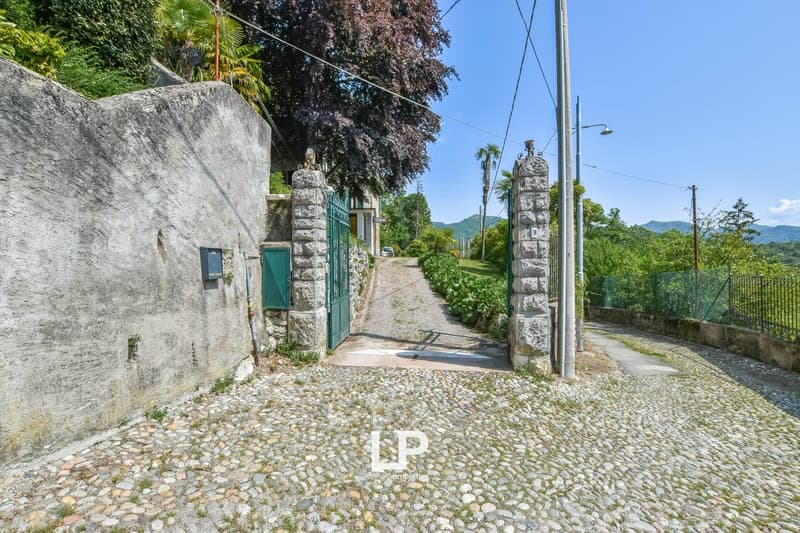 Cobblestone driveway, stone pillars, closed green gate, greenery around, hills in the background