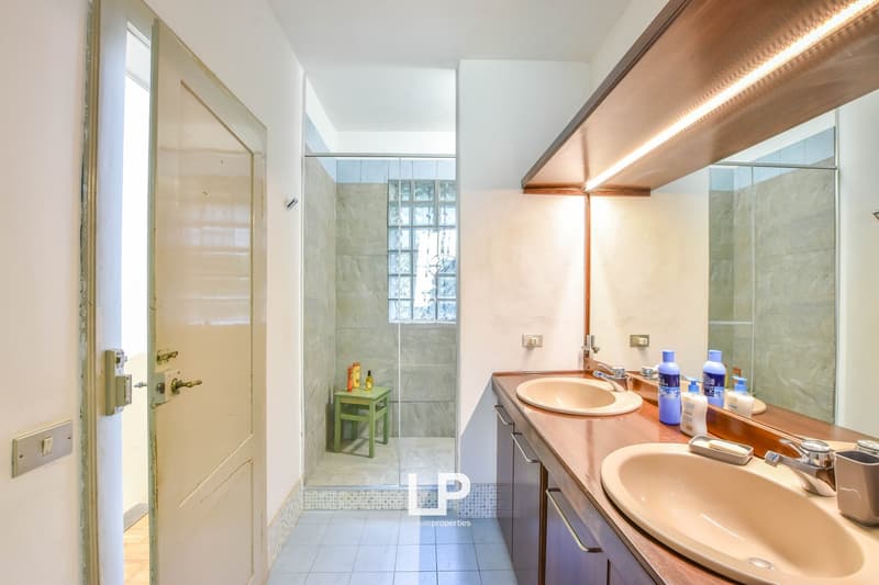 Double sinks, mirror, shower enclosure, wooden shelves, tiled floor