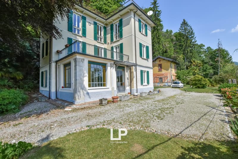 White house with green shutters, balcony, gravel driveway, smaller building, greenery
