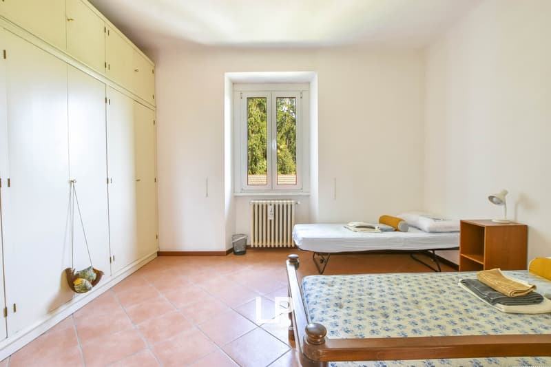Two twin beds, wooden side table, lamps, radiator, white wardrobes, small garbage bin, wooden floors