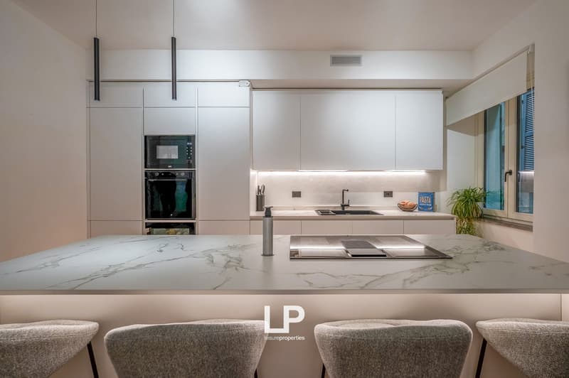 Modern open-plan kitchen with marble countertops, integrated appliances, built-in oven, and dishwasher