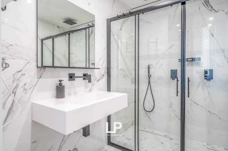 modern bathroom with white tiles, large mirror, walk-in shower, vanity sink, soap dispenser, black fixtures
