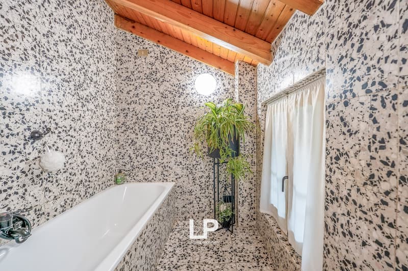 A small bathroom with a white bathtub, grey speckled walls, wooden ceiling, and a white curtain.
