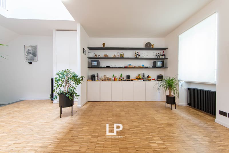 large open space, wooden flooring, shelves with decor items, potted plants, white cabinetry, kitchen appliances, framed picture, glass window