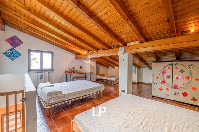bedroom with wooden ceiling, two single beds, wooden table, radiator, window, decorative paintings, and a colorful cabinet