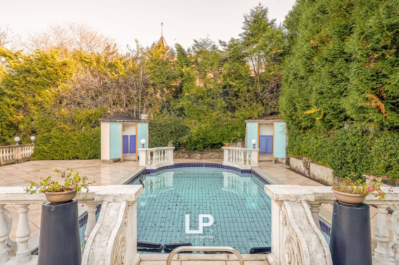 Swimming pool with white railings, green hedges, blue buildings, and trees