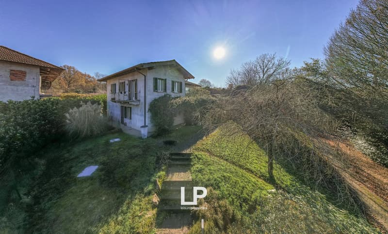 Single-family house on the hill, white exterior, red roof, small garden, stairs leading up to the entrance, surrounded by trees and bushes, balcony