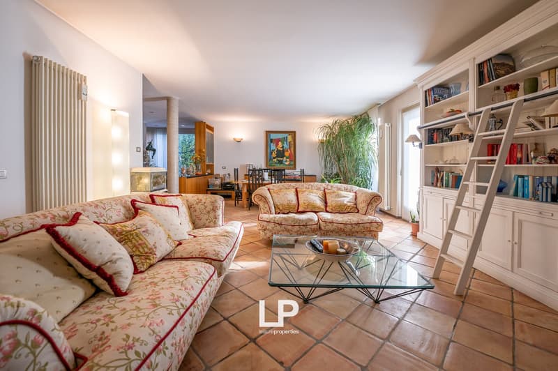 Spacious living room with tiled floor, two sofas, glass table, bookshelves, ladder, potted plant, picture frame on the wall