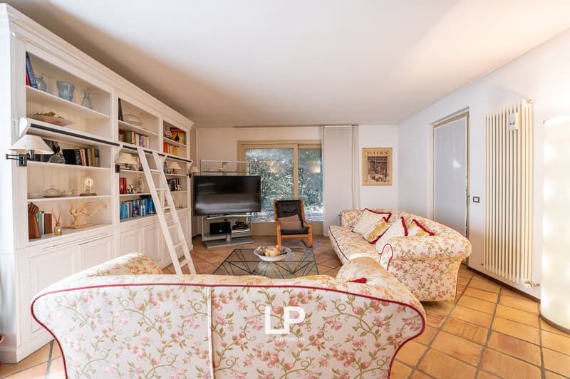 living room, wooden flooring, large white wardrobe, shelves, TV, two floral sofas, glass coffee table, radiator, wooden ladder, wooden armchair