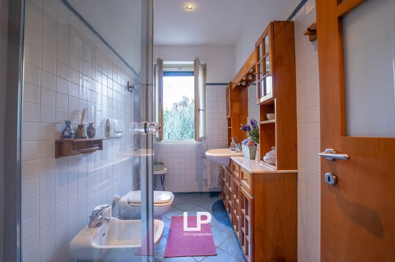 white tiled walls, white floor, double sink, shower enclosure, toilet, wooden cabinets, flower vase