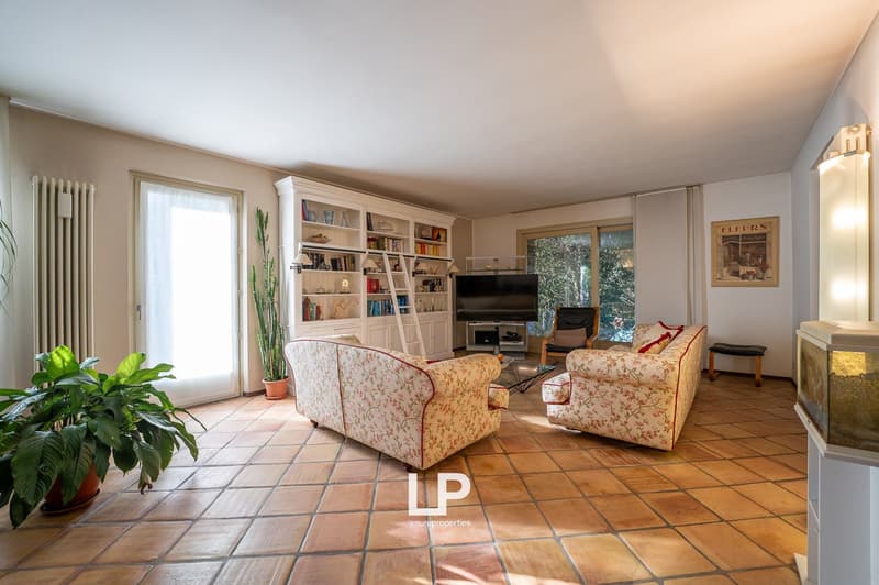 living room with a large window, couch, two armchairs, bookshelves, TV, plants