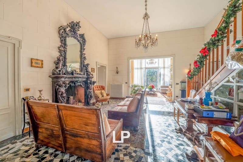 Large living room with wooden furniture, fireplace, ornate mirror, chandelier, tiled floor, radiator
