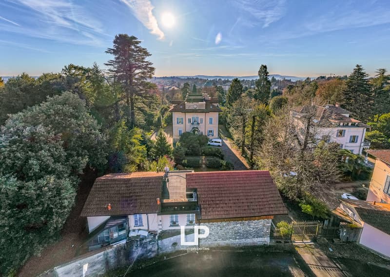 Villa on hill, large, multistory, surrounded by trees, distant city skyline, parked van in driveway.