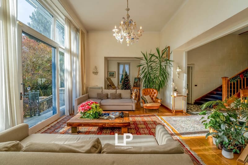 Living room, chandelier, wooden floor, sofa, coffee table, staircase, balcony with railings, large windows, Christmas tree, plants