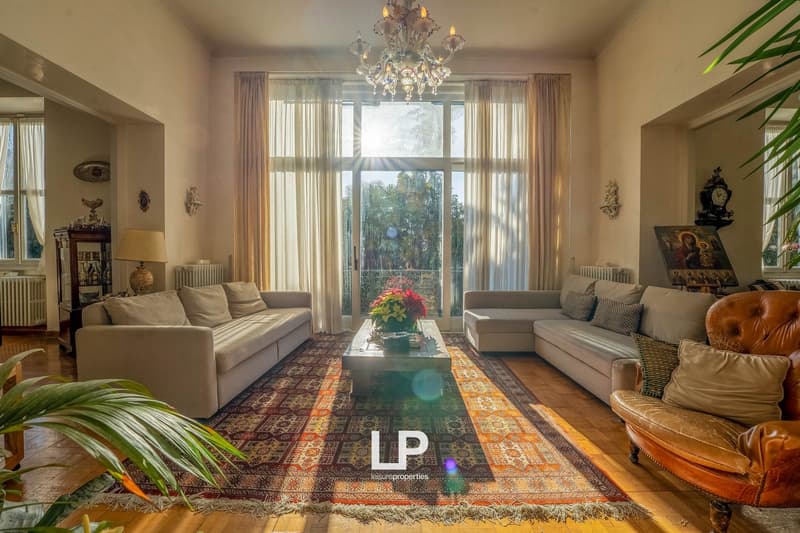 Spacious living room with wooden floors, large windows, glass balcony doors, chandelier, couches, and center coffee table