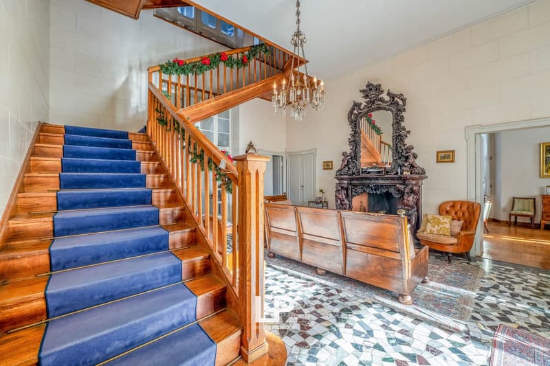 Large staircase, blue carpet, chandelier, wooden furniture, fireplace, mirror, painting