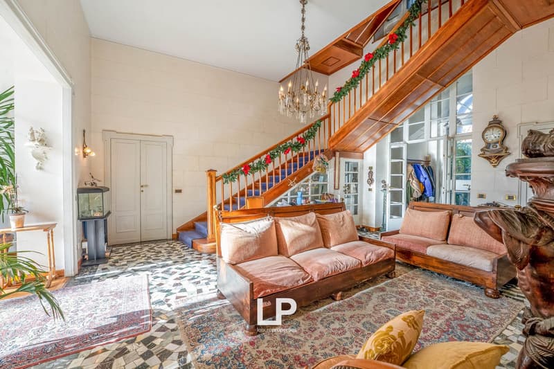 elegant living room, white walls, chandelier, wooden staircase, carpet, two wooden sofas, wooden door
