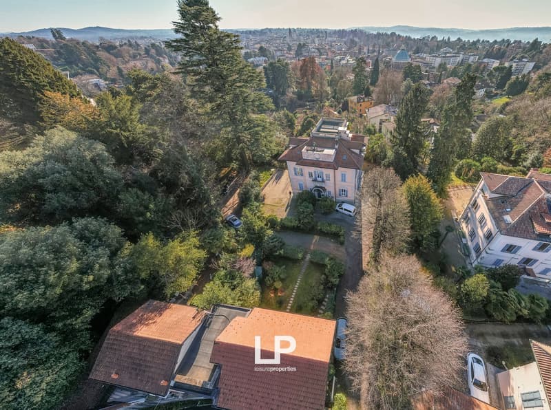 Large villa with red roof, white walls, windows, garage, garden, scenic city view, multiple cars parked
