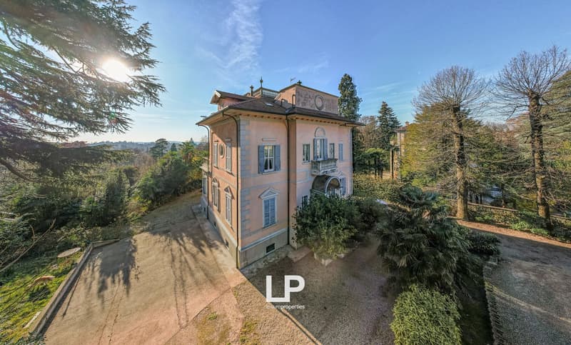 large villa with many windows, beige exterior, surrounded by trees, driveway leading to entrance, two storeys