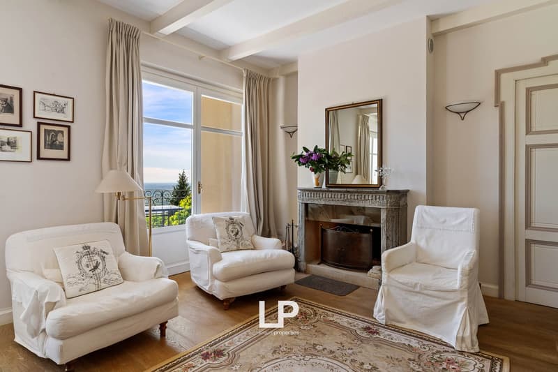 living room with fireplace, large windows, white armchairs, wooden floor, lamps, mirror
