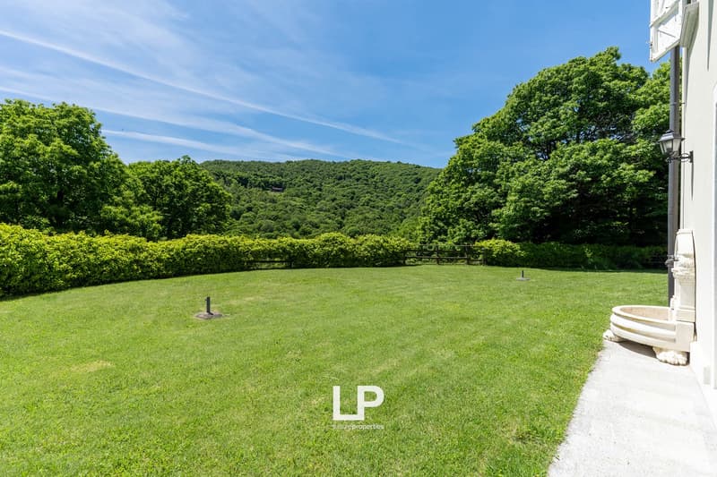large manicured lawn with a hedge, wooden fence, and a mountain view
