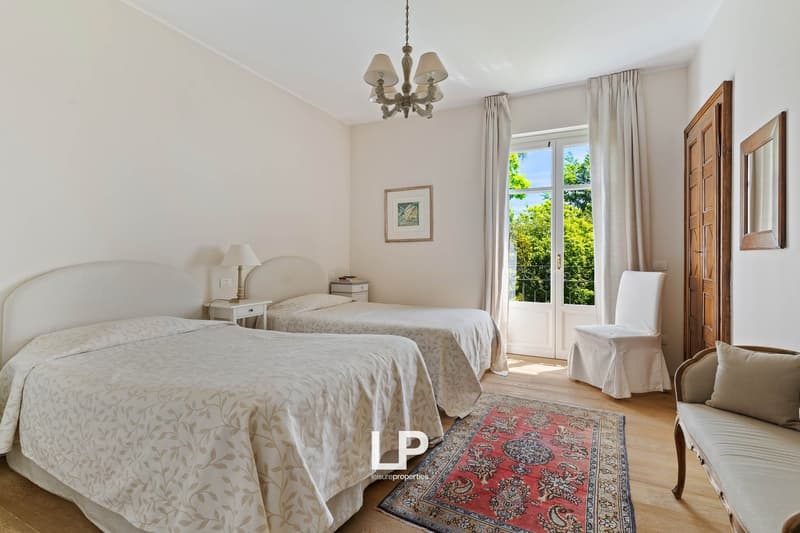 Two twin size beds, bedside tables, picture frame, lamp, rug, wooden door, covered chair, wooden mirror, windows