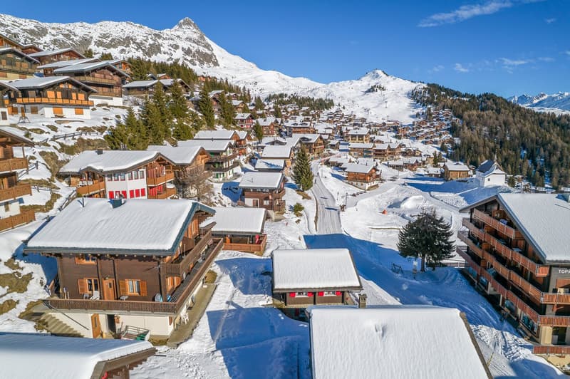 Mountain village with wooden buildings, snowy roofs, surrounded by mountains, winter scenery