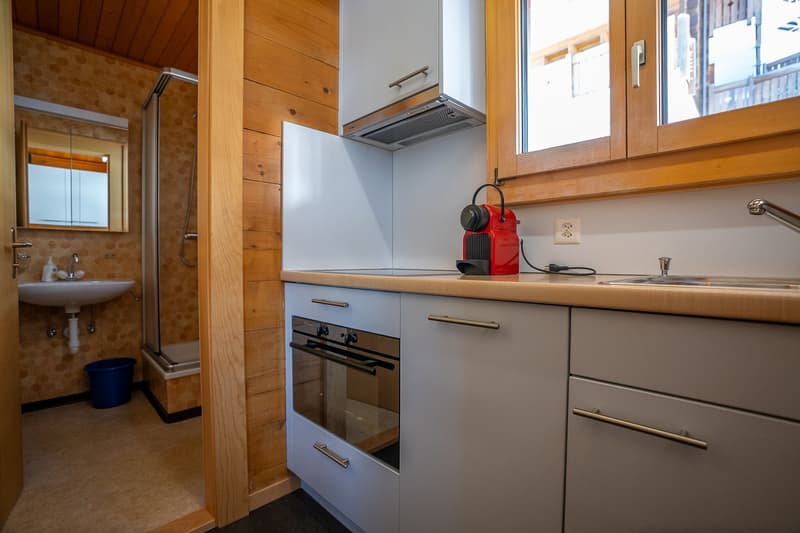 White countertops, oven, sink, wooden cabinets, countertop with an oven extractor and an electric coffee machine, sink faucet, and an electrical outlet.