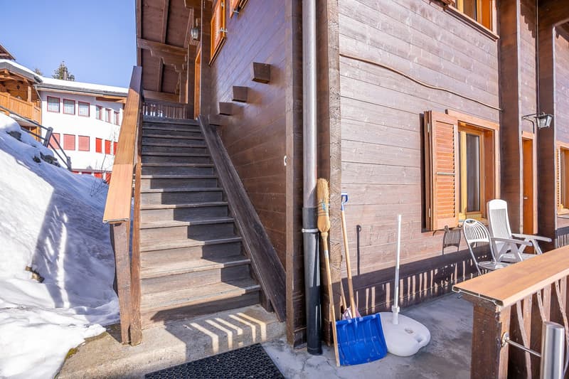 2 story wooden house, red shutters, stairs to entrance, covered front deck, snow-covered area