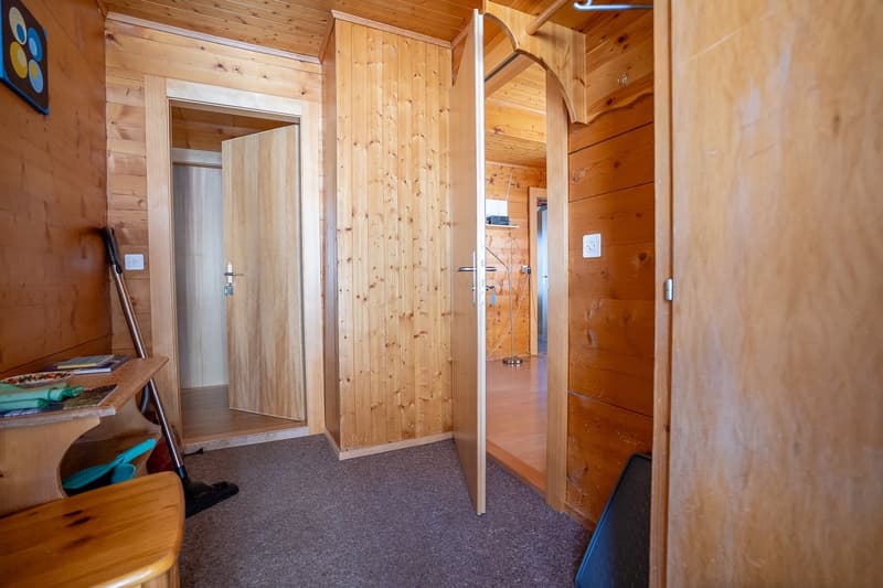 wooden walls, carpeted floor, wooden table with books and plates, broom leaning on wall, open doors