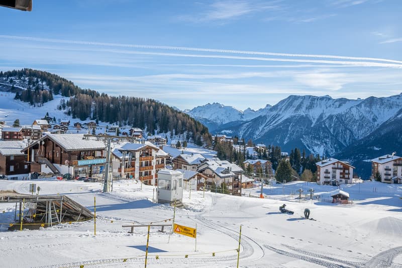 Buildings, ski slopes, people skiing, mountains in the background