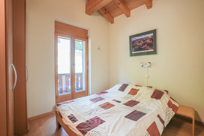 Bedroom with a double bed, wooden closet, wooden flooring, a picture frame, double doors with balcony, night lamps.
