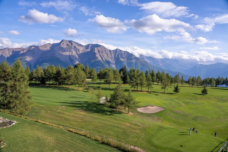 Golf course with several fairways, sand traps, fairway bunkers, trees and lush green grass, mountains in the background