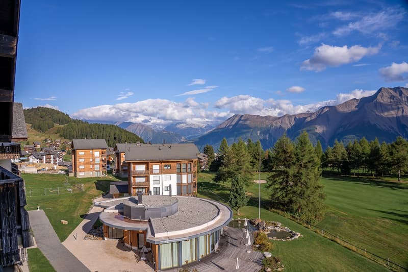 Mountain lodge building, circular design, green landscape, golf course, surrounded by trees