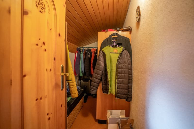 Storage room with wooden wardrobe, jackets hanging, storage bench, and a wooden door.