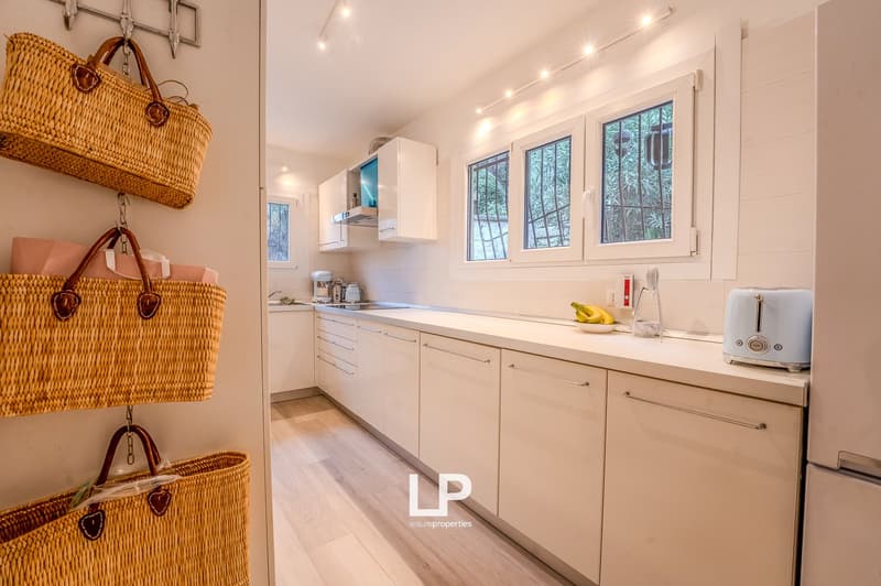 White kitchen with a gas stove, two basket holders with wicker baskets, microwave, toaster, refrigerator and window with grill