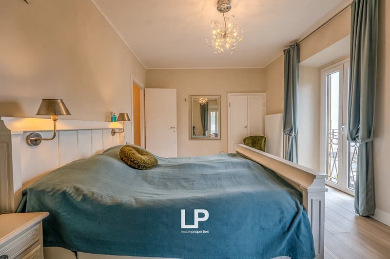 a cozy bedroom with double bed, lamps, wooden floor, and windows with curtains
