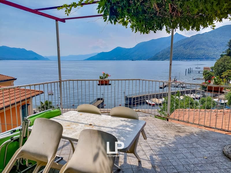 Outdoor balcony with metal railings, table, chairs, plants, lake view, mountains