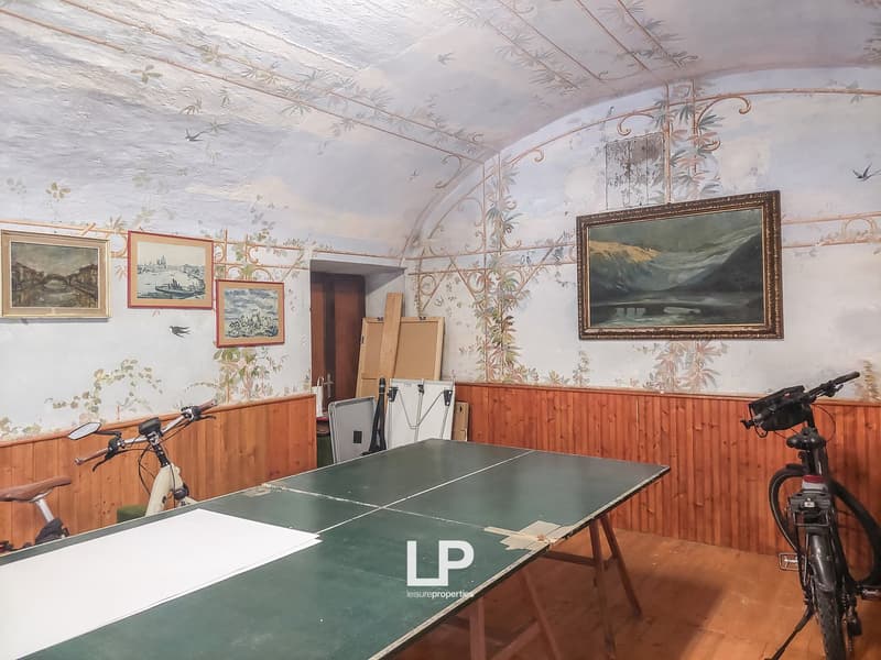 A room with wall paintings and pictures, a green table, bicycles, and a folded chair.