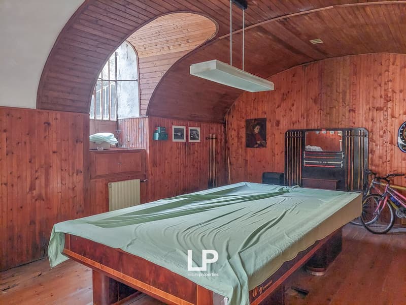 vaulted ceiling, wood walls, pool table, bicycles, arch window, arched window, pool cue rack, hanging lamp, radiator
