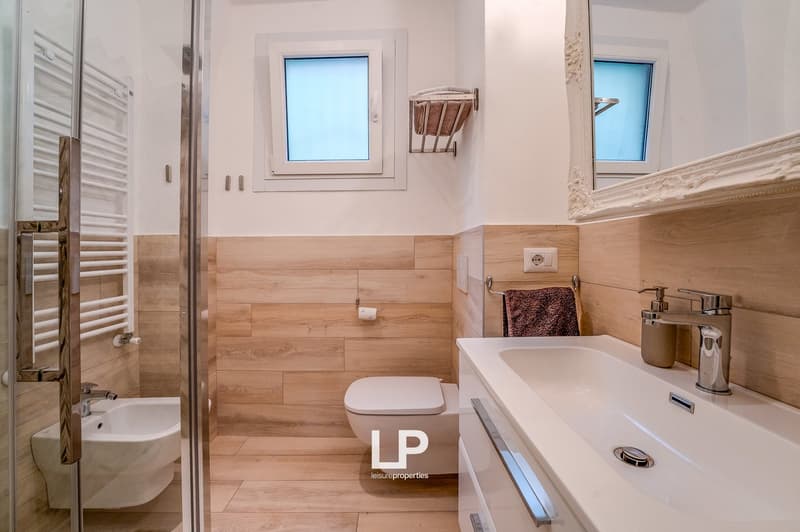 Bathroom: wooden floor, white walls, white bathroom fixtures, walk-in shower, toilet, mirror, sink, towel rack