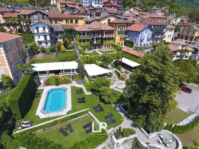 Outdoor area with a swimming pool, sun loungers, trees, and hedges. A white canopy is positioned over the swimming pool.
